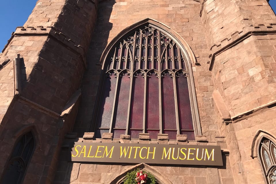 The exterior of the Salem Witch Museum, featuring Gothic architecture with pointed arches and a large stained glass window.