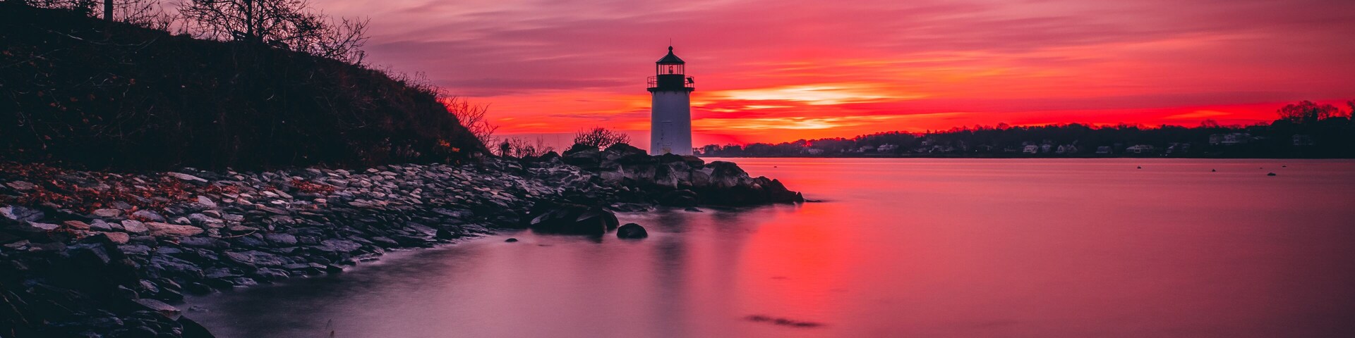 Un faro en una costa rocosa al atardecer, con un cielo vibrante.