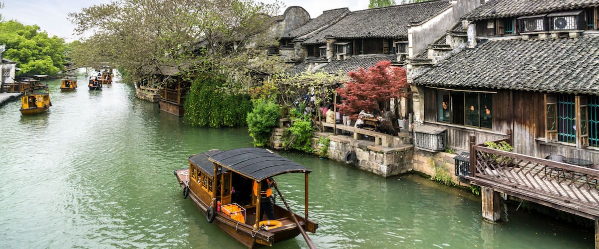 A traditional wooden boat on a river, surrounded by historic buildings with tiled roofs.