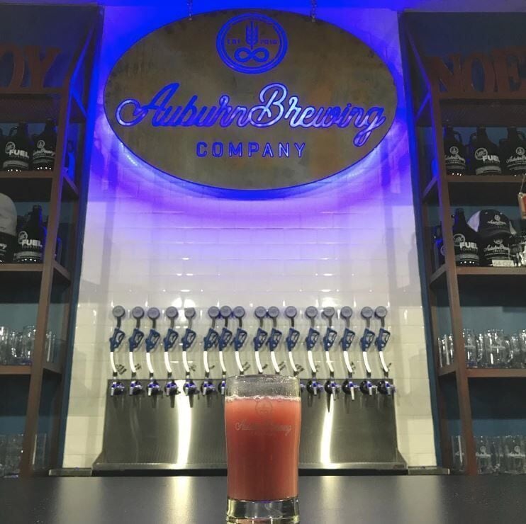 A bar with a sign for Auburn Brewing Company and a tap of a red beverage.