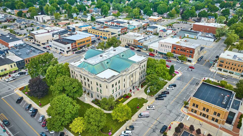 An aerial view of a town with a prominent historic building with a green roof, surrounded by smaller commercial buildings and streets.