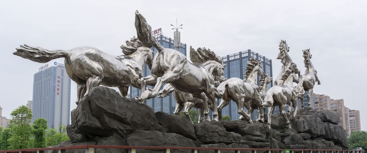 A large metallic sculpture of horses on rocks with a cityscape in the background.