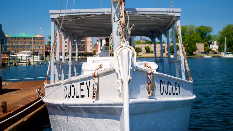 A white boat named 'DUDLEY' docked at a marina with buildings and trees in the background.