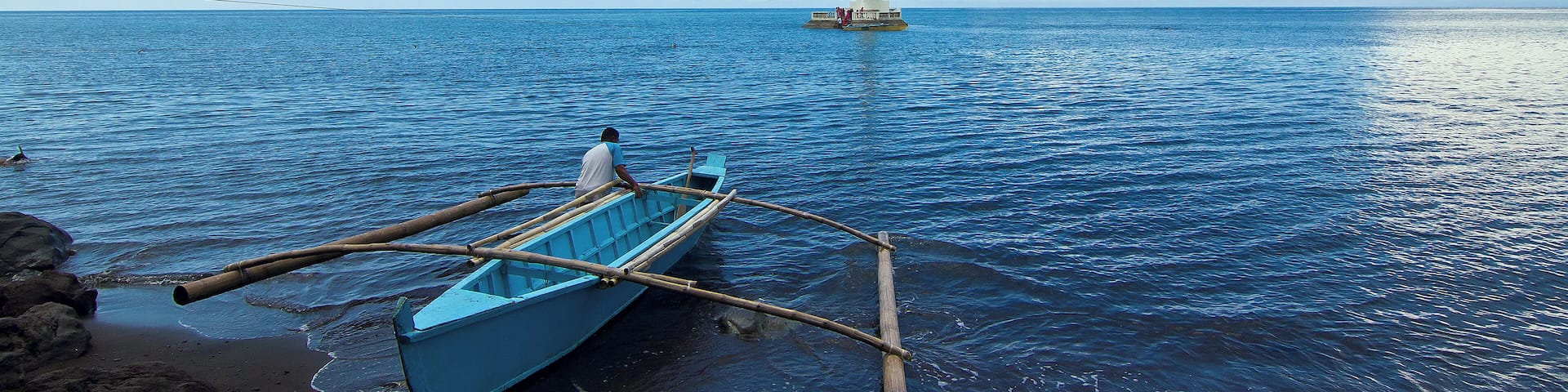 A local pushes his boat to the open sea towards the lone, conspicuous cross that marks the old cemetery of Camiguin island that was sunk in one of the island volcano's eruption more than a century ago.
