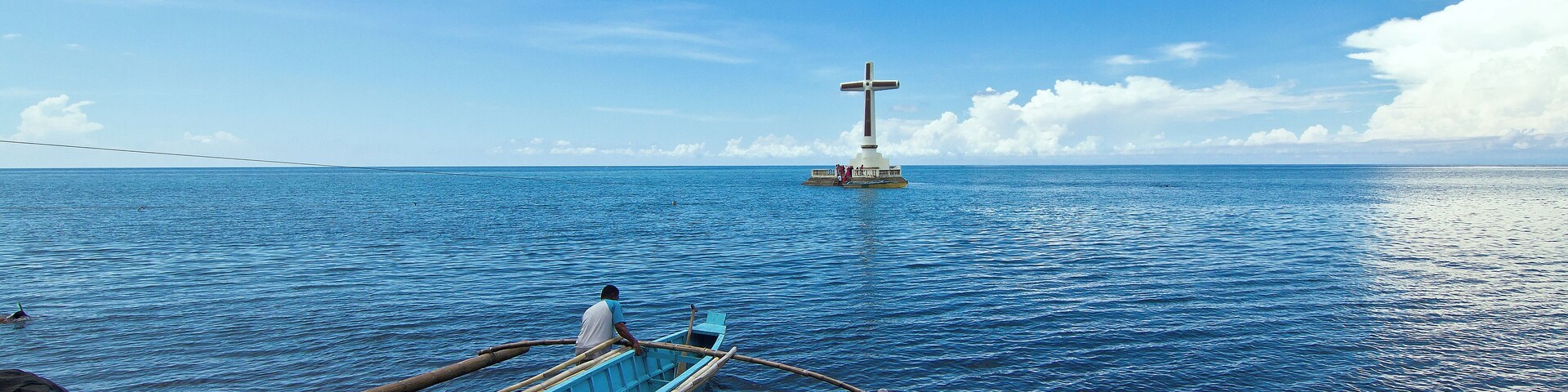 A local pushes his boat to the open sea towards the lone, conspicuous cross that marks the old cemetery of Camiguin island that was sunk in one of the island volcano's eruption more than a century ago.