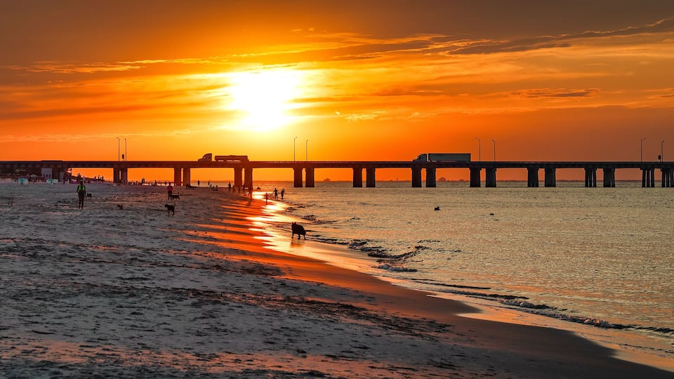 A beach at sunset with a pier extending into the water.