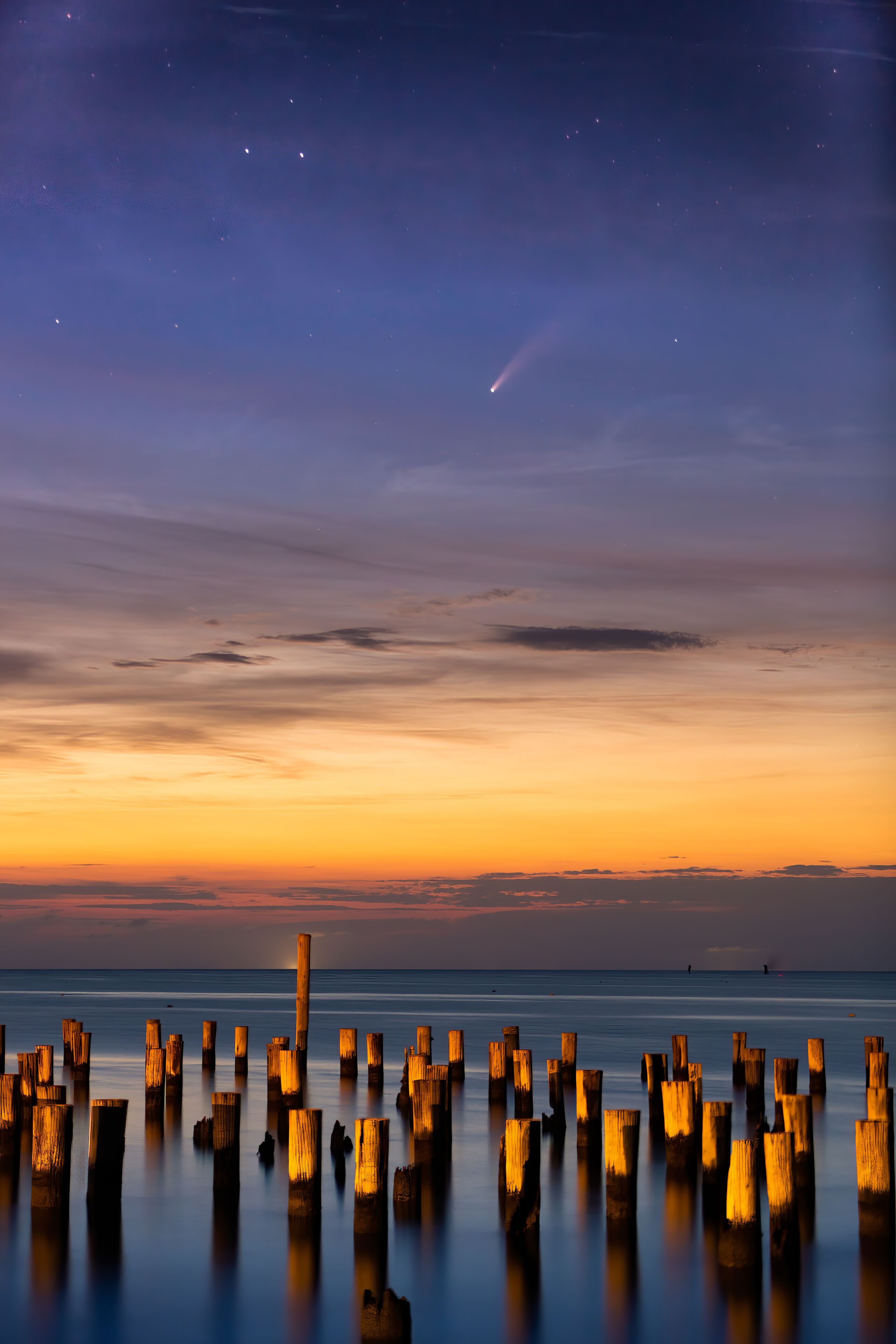 A sunset over a calm sea with wooden posts in the foreground.