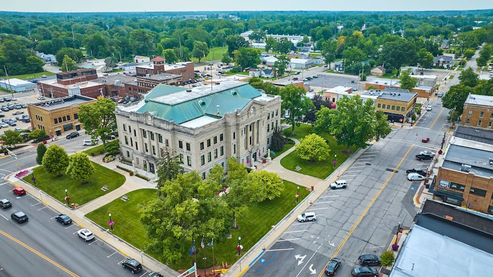 A cityscape with a prominent historic building with a green roof, surrounded by lush green trees and a wide street.