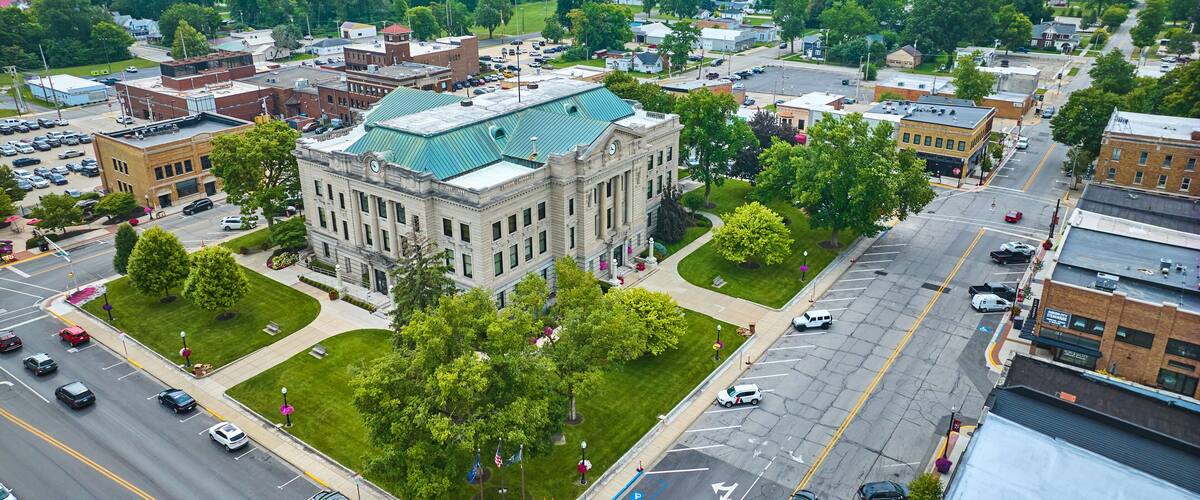 A cityscape with a prominent historic building with a green roof, surrounded by lush green trees and a wide street.