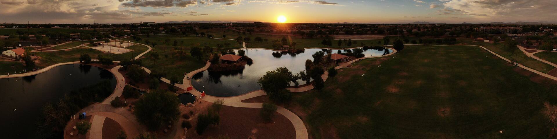 A sunset over a park with a lake, pathways, and distant buildings.