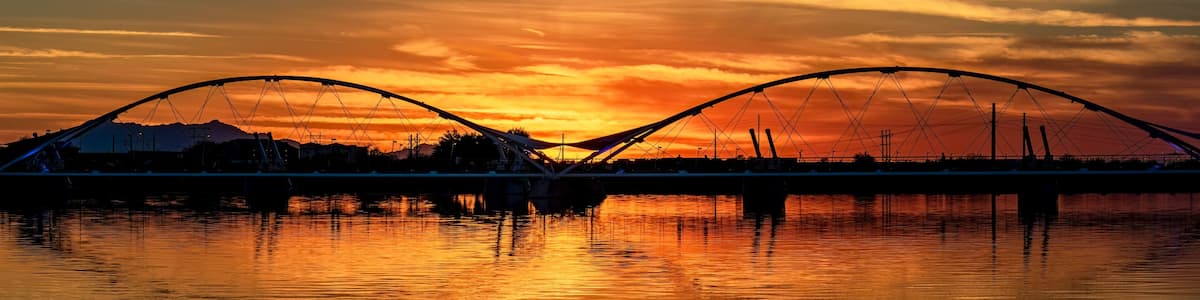 A sunset over a river with a bridge and mountains in the background.