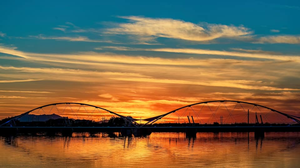 A sunset over a river with a bridge and mountains in the background.