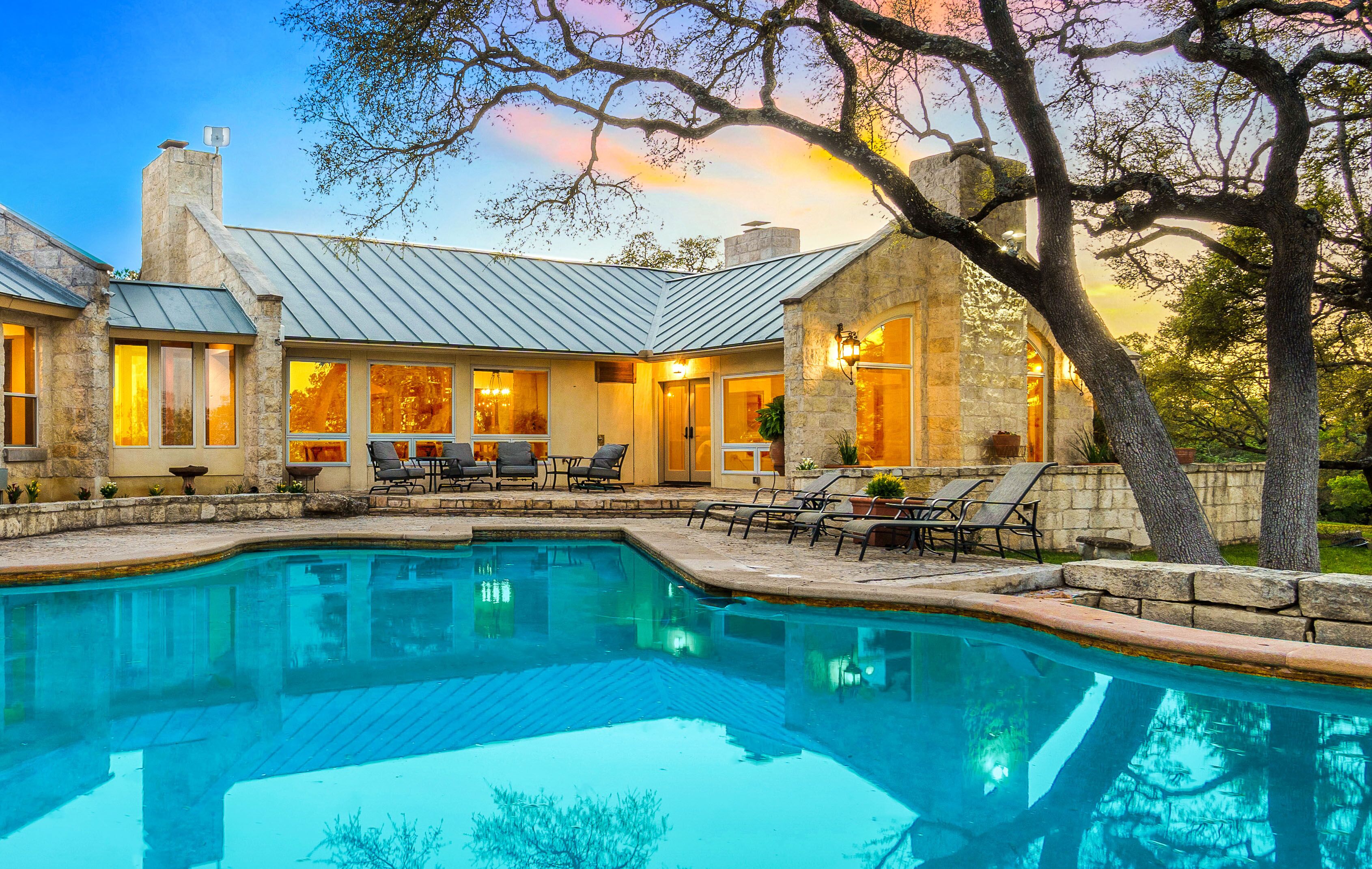 A stone house with a swimming pool, outdoor seating, and trees.