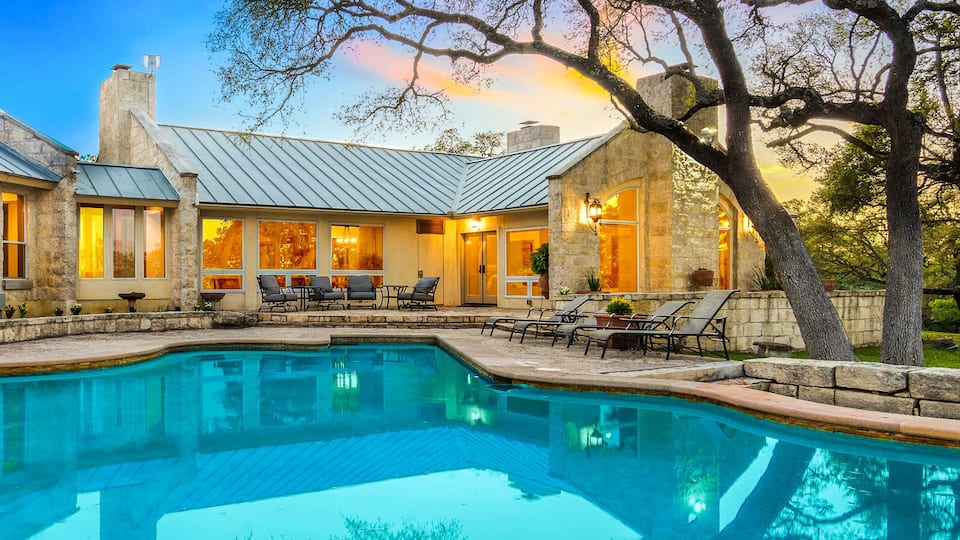 A stone house with a swimming pool, outdoor seating, and trees.