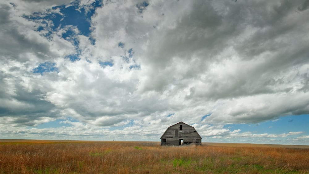 A solitary barn in a vast field under a dramatic sky.