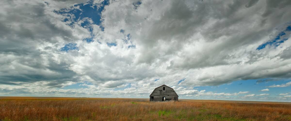 A solitary barn in a vast field under a dramatic sky.