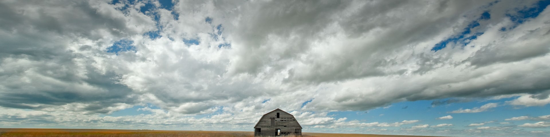 A solitary barn in a vast field under a dramatic sky.