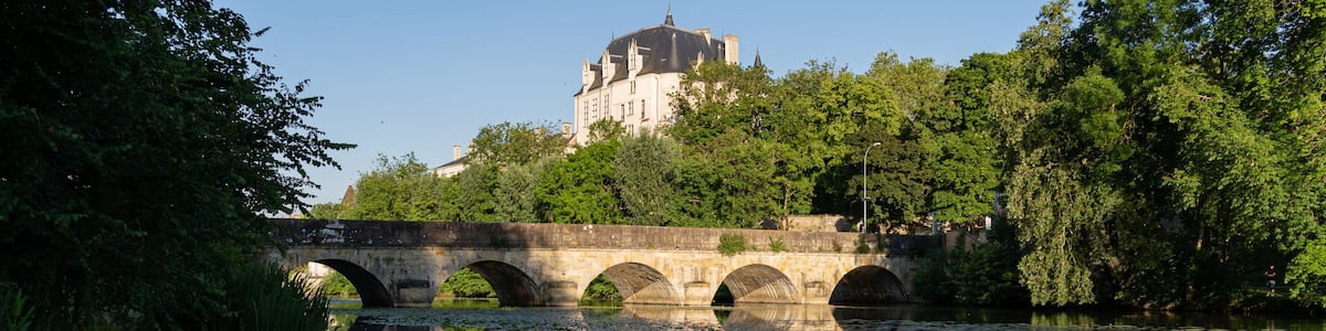 A stone bridge over a calm river with a castle in the background.