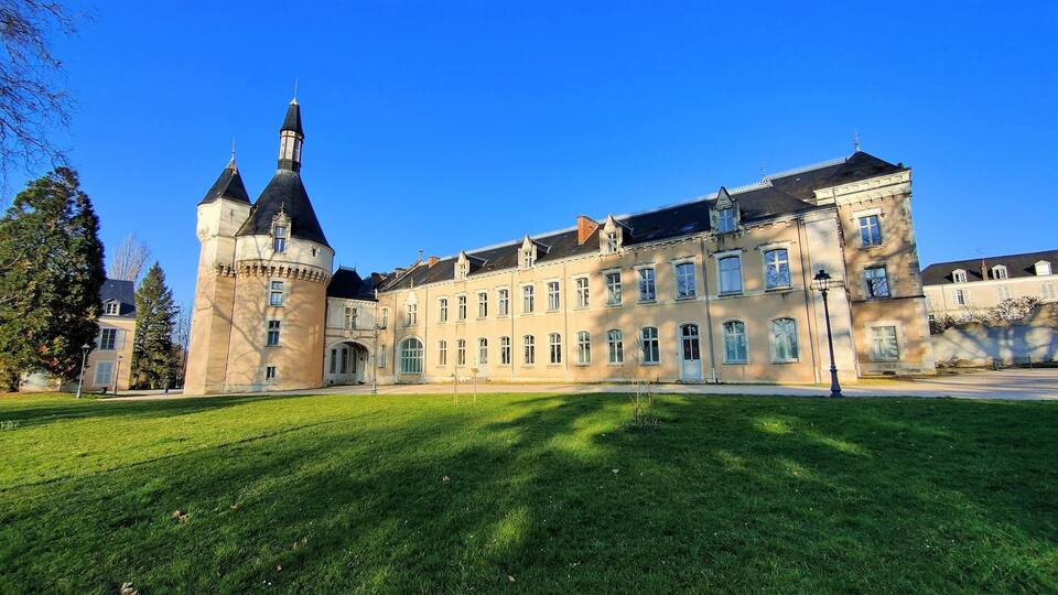 A large historic building with a prominent tower and a well-maintained lawn.