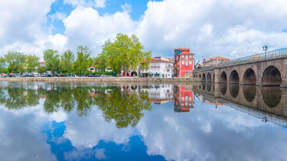 A stone bridge over a calm river reflecting trees and buildings.