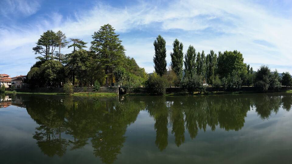 A serene lake with reflections of trees and a building with a red roof.