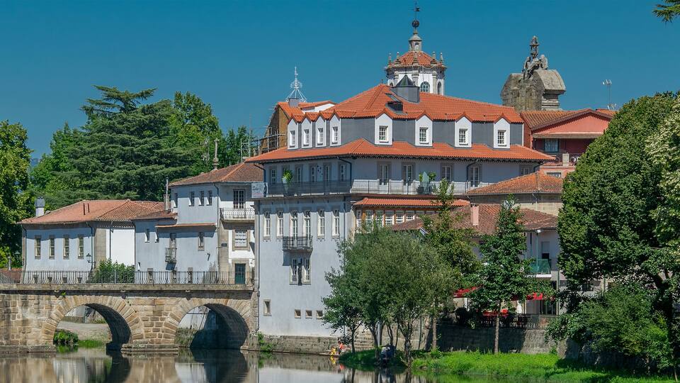 A historic building with a red-tiled roof and a bridge over a calm river.