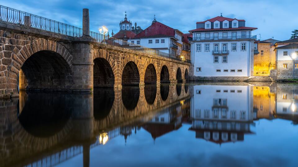 A stone bridge with arches over a calm river, reflecting the surrounding buildings.