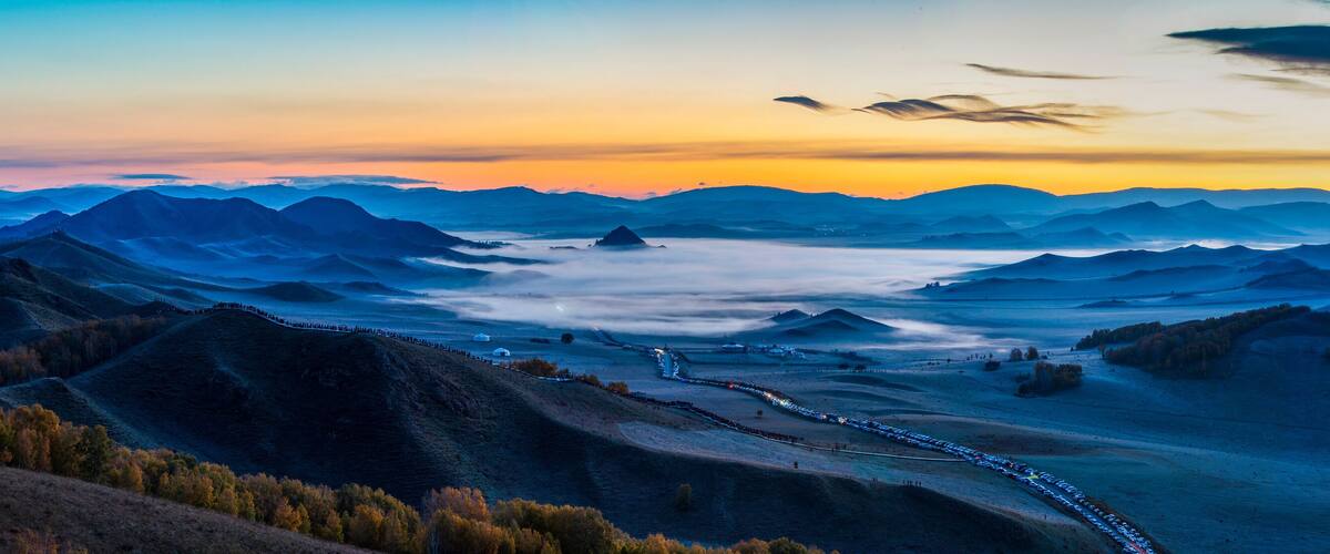 A mountainous landscape with a winding road and a line of vehicles.