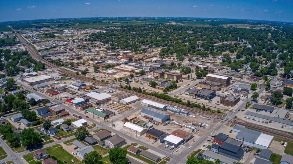 An aerial view of a town with a railway line, industrial buildings, and surrounding greenery.