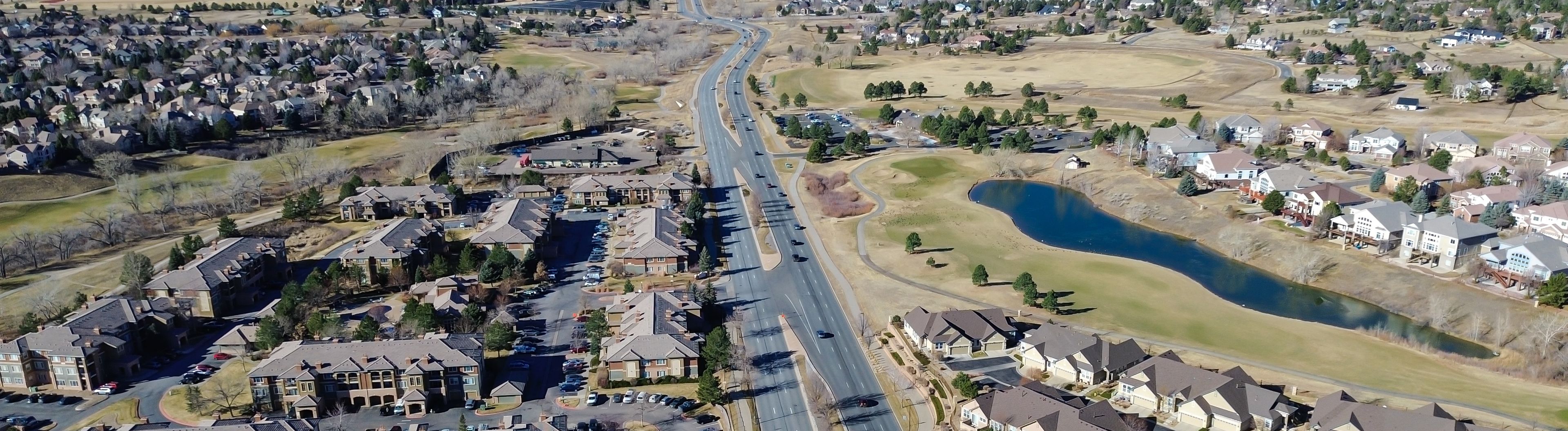 Panorama view apartment clusters sit along the golf course edge south of busy E Arapahoe Rd with open fairways beyond. Neutral siding, winter turf, leafless trees muted scene, Aurora, Colorado