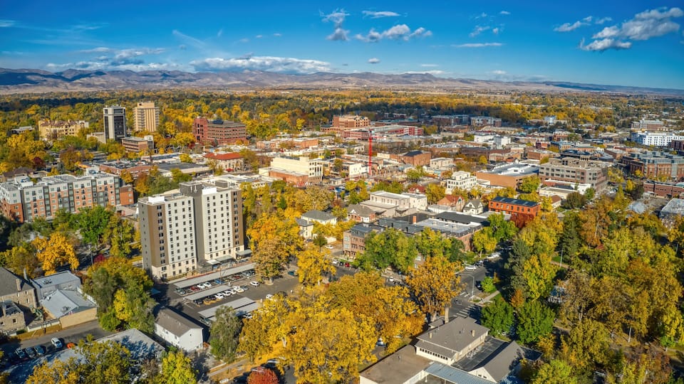 A cityscape with autumn foliage, buildings, and mountains in the background.