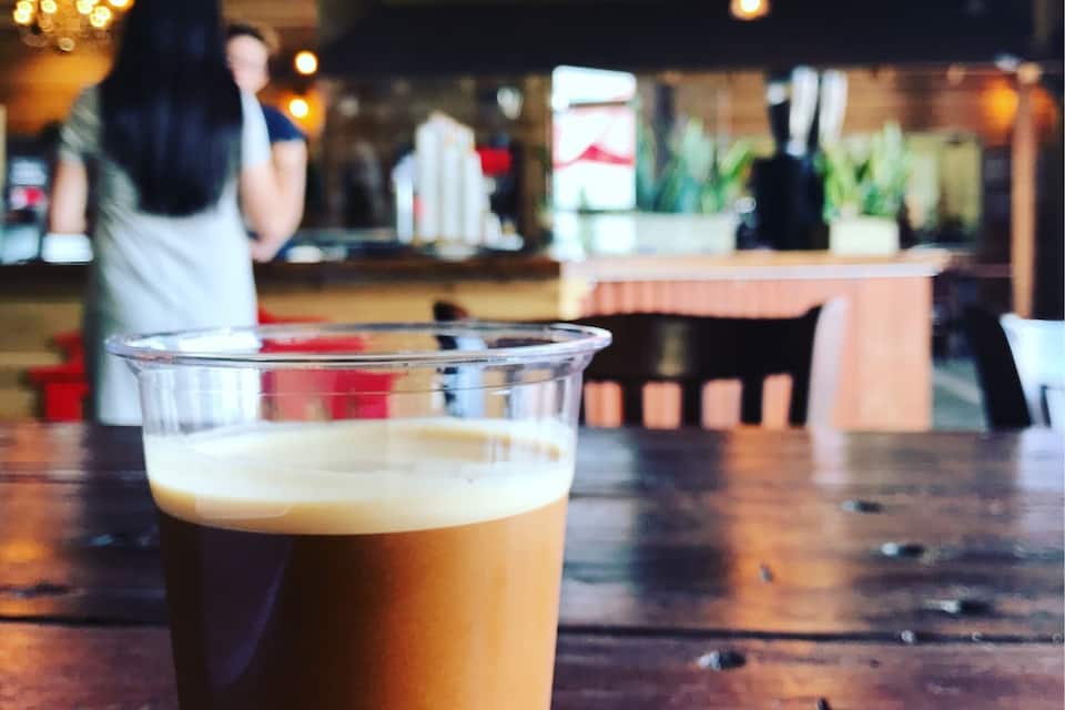 A glass of iced coffee on a wooden table with a blurred background of a cafe interior.