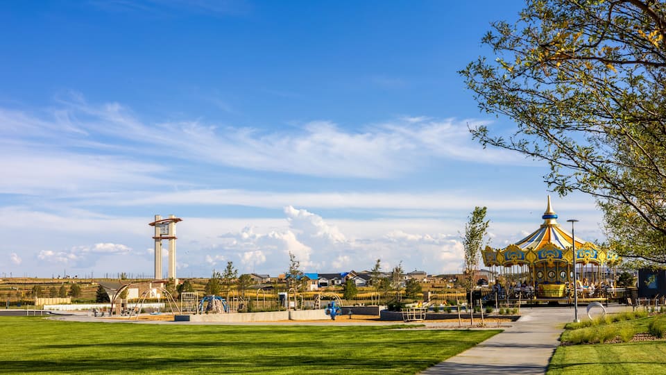 A park with a carousel, a tall tower, and a clear blue sky.