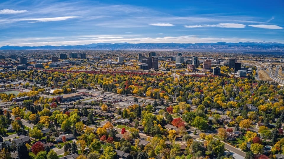 An aerial view of a city with autumn foliage, a highway, and distant mountains.