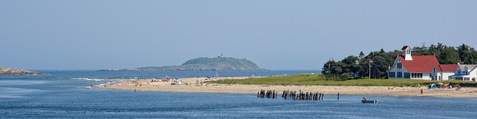 Escena costera con una playa arenosa, un faro y una casa de techo rojo.