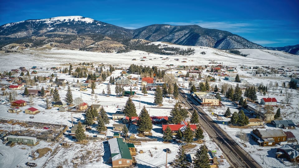 A snow-covered town with a railway track, surrounded by mountains and pine trees.