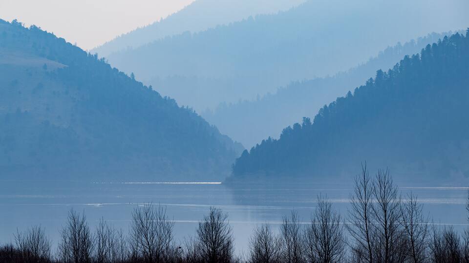 A calm lake surrounded by forested hills.