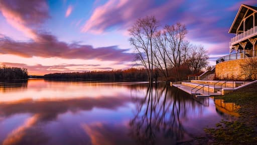 A serene lake with a sunset, trees, and a stone building with stairs.