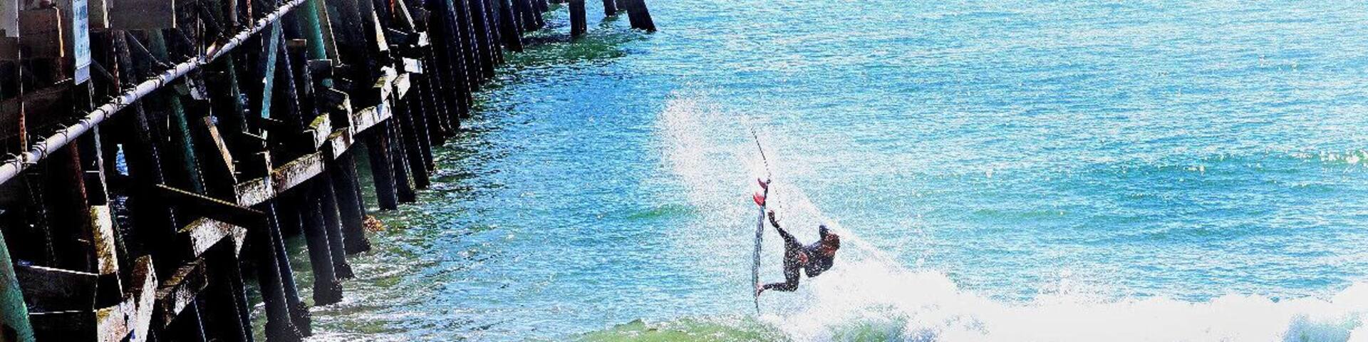 Un surfista cabalgando una ola cerca de un muelle.
