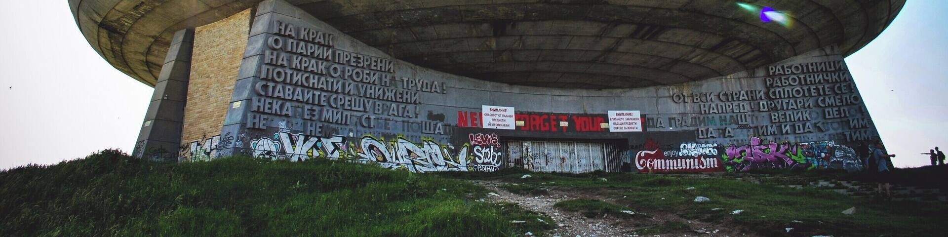 A large, circular concrete structure with graffiti and signs, surrounded by grass and hills.