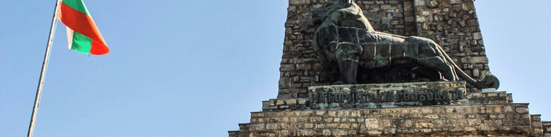 A stone tower with a lion statue at the top, a flagpole with a flag, and a staircase leading up to the entrance.