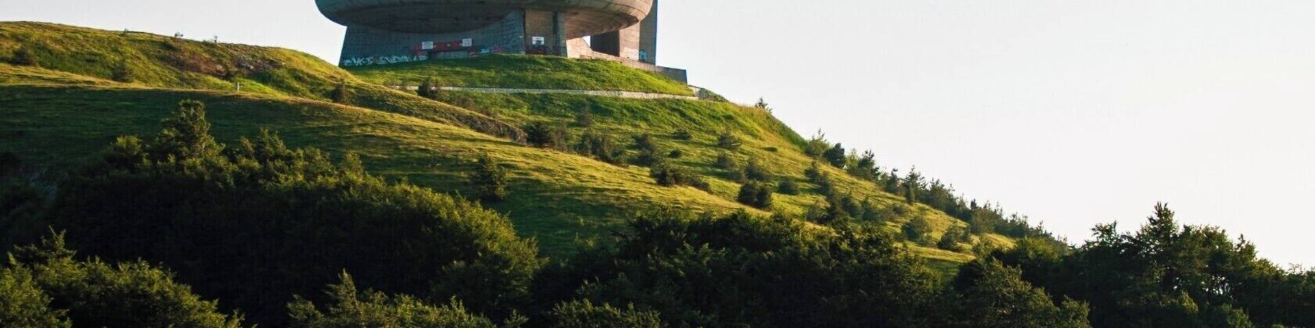A tall tower and a circular building on a grassy hill.
