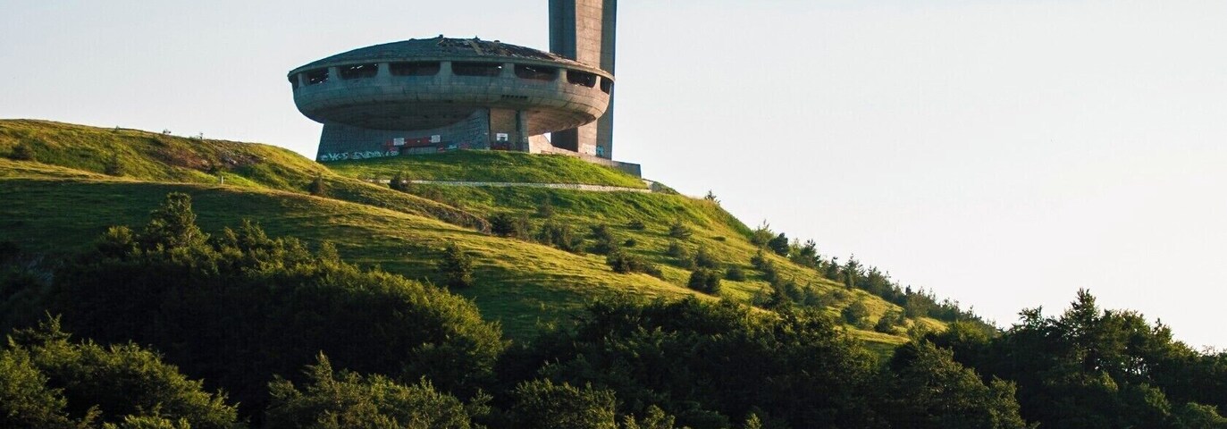 Uma torre alta e um edifício circular numa colina coberta de relva.