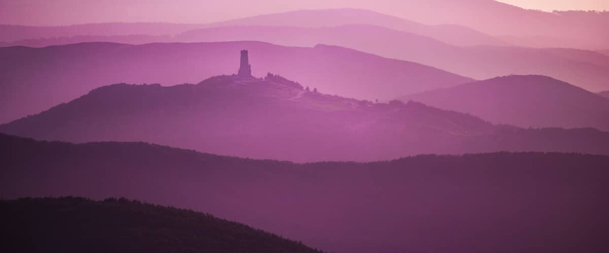 A mountain range with a prominent hill featuring a tower-like structure.