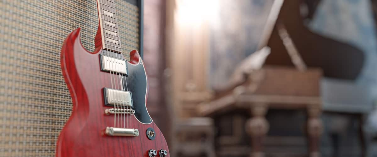 A red electric guitar leaning against a speaker in a room with a piano in the background.