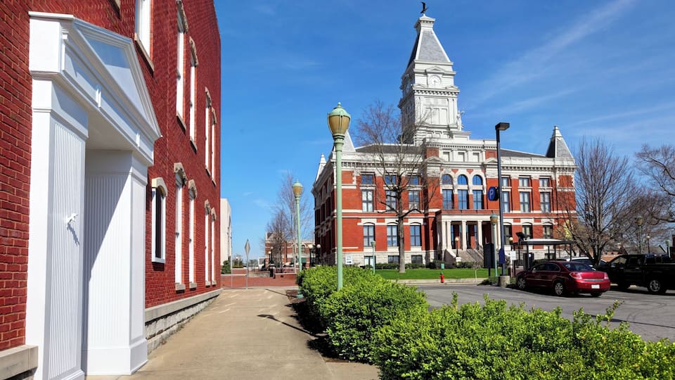A red brick building with white trim, a clock tower, and a parking lot.