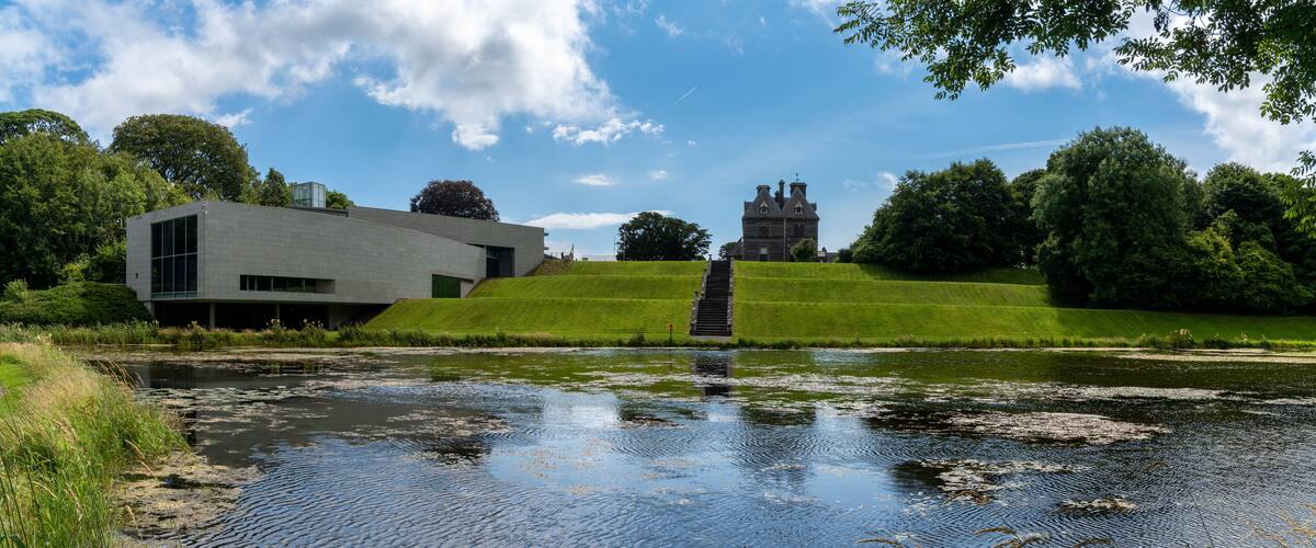 A modern building, a traditional house, and a grassy hill with a pond.