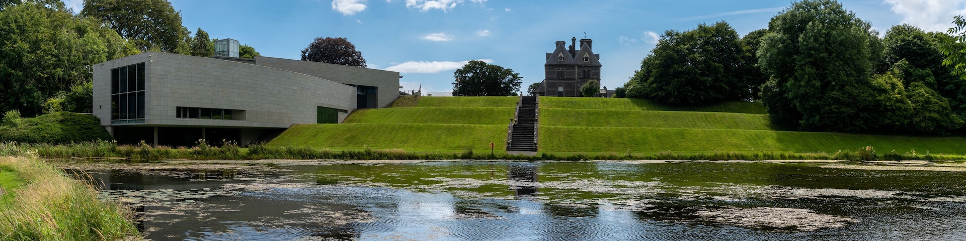 A modern building, a traditional house, and a grassy hill with a pond.