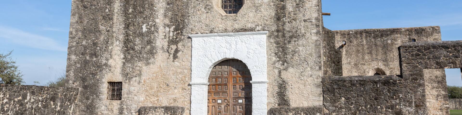 Una iglesia histórica de piedra con un campanario, una entrada de arco y una cruz en la parte superior.