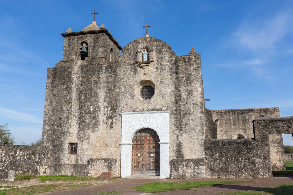 A historic stone church with a bell tower, arched entrance, and a cross on top.